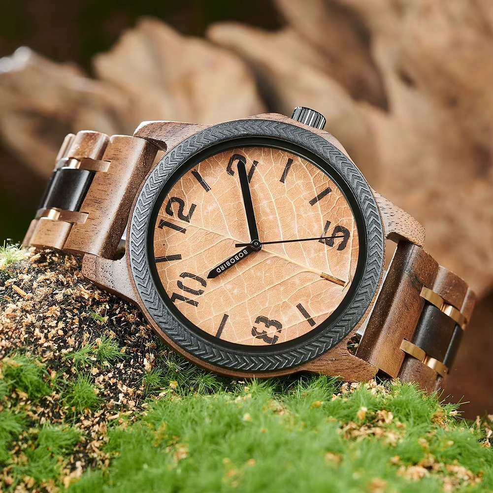 Montre Ambre en bois de noyer avec cadran motif feuille et lunette noire, chiffres arabes visibles, bracelet bois et détails noirs