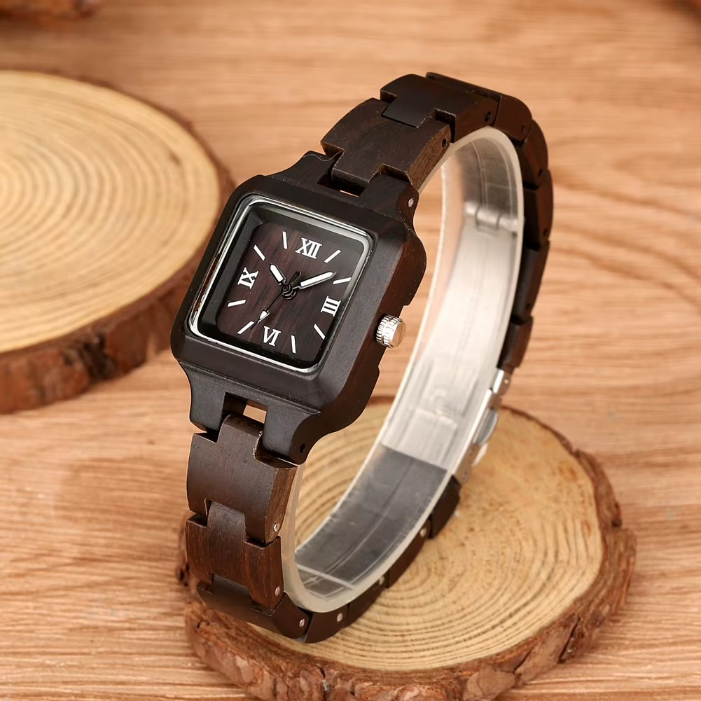 Montre en bois femme Lucerne avec cadran carré 26 mm et bracelet fin en bois foncé posée sur rondins de bois
