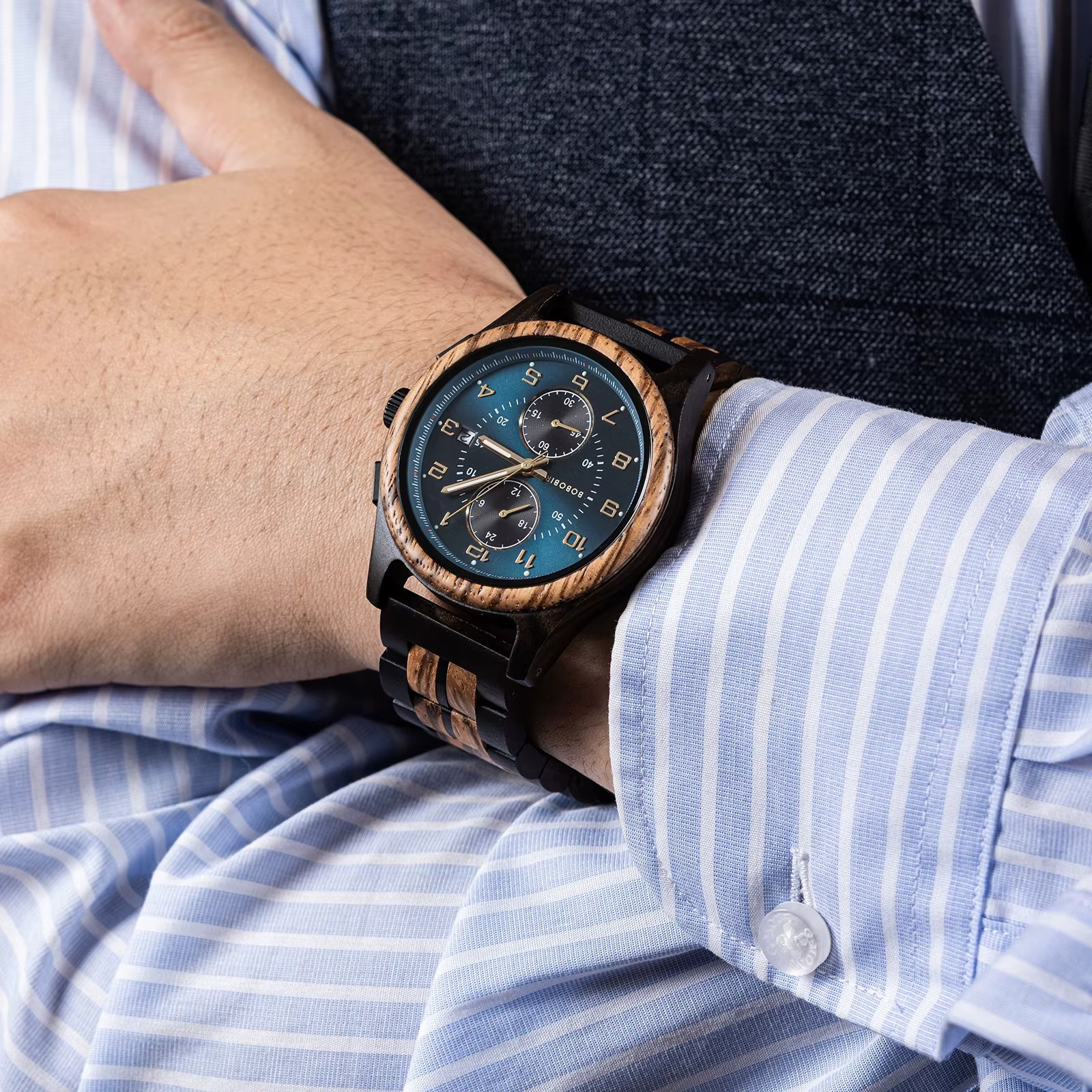 Montre en bois Santorin chronographe avec cadran bleu et ébène portée au poignet d'une personne en chemise rayée bleue