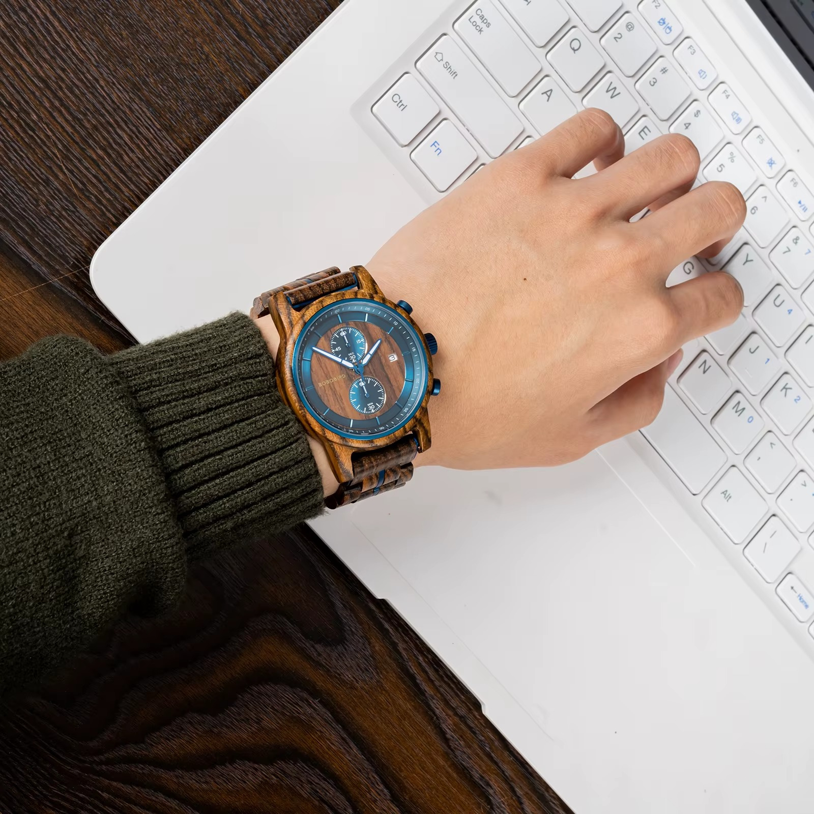 Montre Delphes en bois d'olivier et ébène avec cadran bleu et chronographe portée au poignet sur clavier d'ordinateur