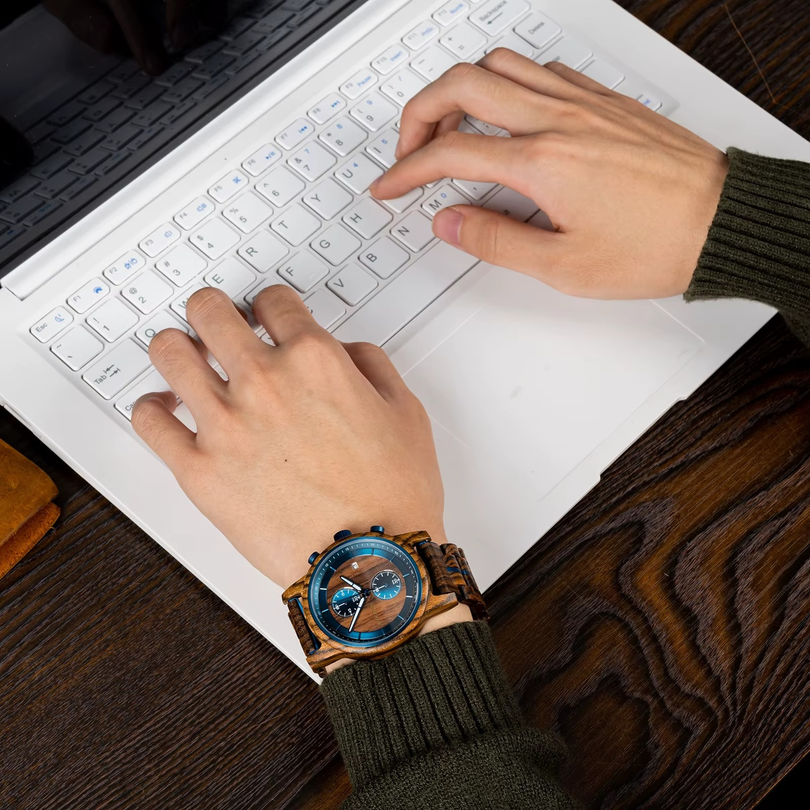 Montre Delphes en bois d'olivier et ébène avec cadran bleu portée au poignet d'une personne tapant sur un clavier blanc