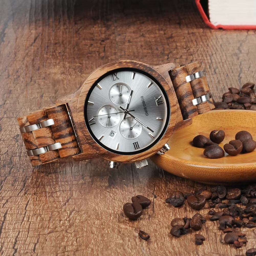 Montre homme Manhattan en bois zébrano et acier avec cadran chronographe argenté vue de face posée sur surface en bois à côté de grains de café