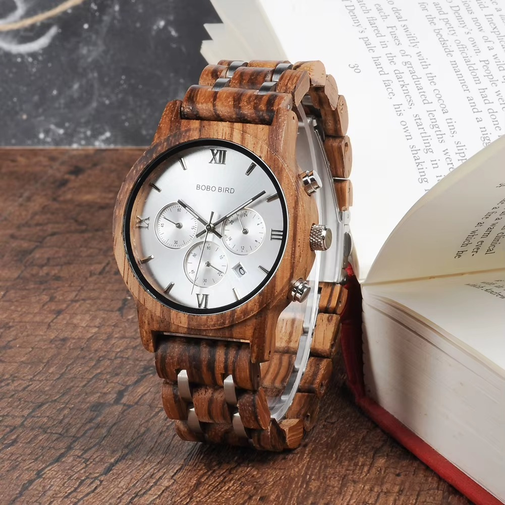 Montre homme Manhattan en bois zébrano et acier avec cadran blanc et chronographe vue de face posée sur une table en bois à côté d'un livre ouvert