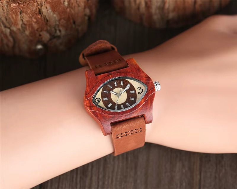 Montre en bois mixte modèle Nazar avec boîtier en bois rouge en forme d'œil et bracelet en cuir marron portée au poignet